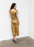 Woman wearing a fashion designer Adrian Hailwood gold metallic dress against a white wall.